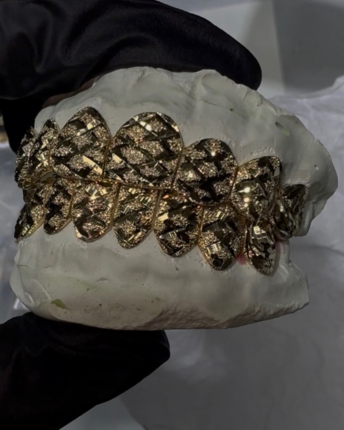 Diamond-cut gold grillz on a dental cast held with black gloves