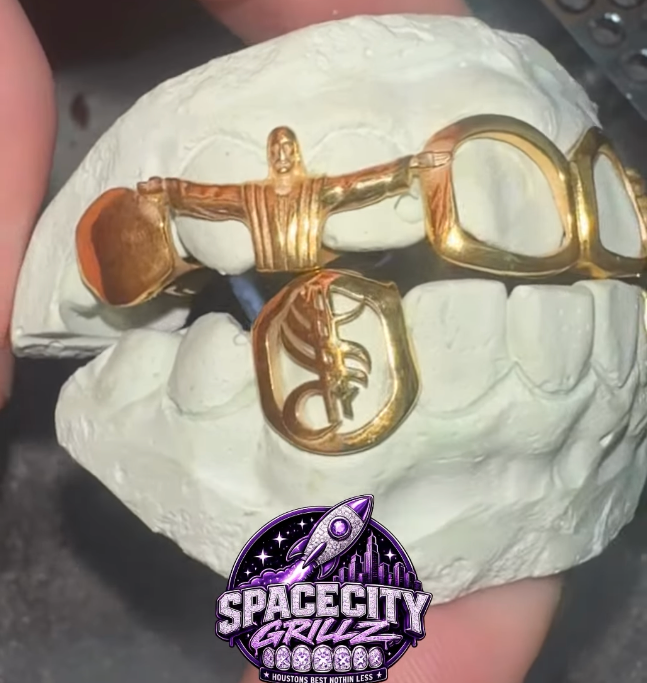 Gold grillz on a white dental plaster mold — a Jesus figure, solid gold cap, open-face window grillz, and a cut-out single cap